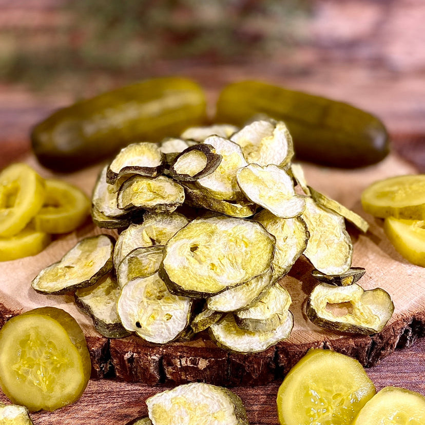 Base Camp Treats Freeze Dried pickles on a wooden board with fresh pickles in the background