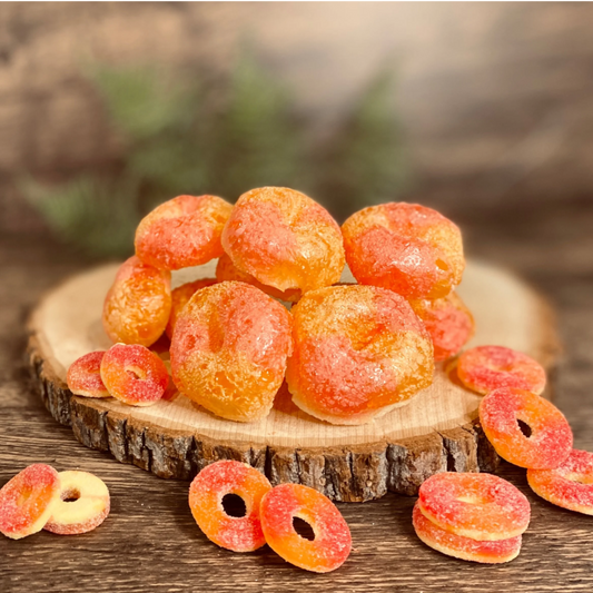 Base Camp Treats Peak Rings Freeze Dried Peach Rings on a wooden disk with a blurred nature themed background